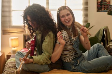 Genç çift yatakta oturuyor, gitar çalarken gülümsüyor ve müziğin tadını çıkarıyor. Pencereden gelen doğal ışık sahne için sıcak ve sıcak retro ortam sağlar