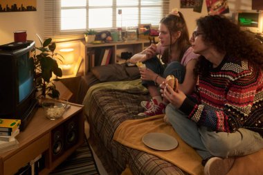 İki arkadaş yatakta oturmuş televizyon izliyor, dondurma ve sandviç yiyorlar, etrafı sıcak retro yatak odalarıyla çevrili. Sıcak ışık rahat bir atmosfer yaratıyor