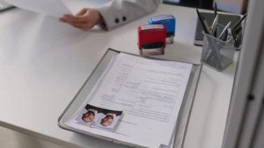 Anonim vize memurunun masadaki vize başvuru formlarını incelerken yüksek açılı görüntüsü ve modern elçilikte reddedilmiş ve onaylanmış pullar.