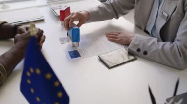 Kimliği belirsiz vize memurunun belgeleri mühürleyip başvuru sahiplerine teslim etmesi ve Schengen vizesini AB büyükelçiliğinde almaları için tezahürat yapması.