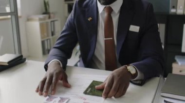 İş günü ABD elçiliğinde çalışan takım elbiseli ve gözlüklü Afro-Amerikan erkek konsolosluk görevlisinin eğik portresi.