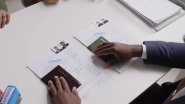 Kimliği belirsiz siyahi erkek vize memurunun evli çiftlere vize uygulamasını onaylaması ve konsolosluktaki görüşme sırasında belgelerini geri vermesi.