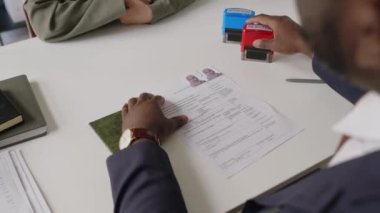 Başvuru formunu reddeden isimsiz vize memurunun omuz üstü fotoğrafı, konsolosluktaki görüşme sırasında Müslüman başvuru sahibine pul yapıştırmak ve belgeleri iade etmek.