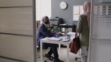 Tam tesettürlü Müslüman bir kadının büyükelçilikteki siyah konsolosluk görevlisiyle röportaj yapmak için vize ofisine girmesi.
