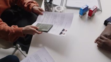 Konsolosluktaki görüşme sırasında kimliği belirsiz bir kadının belgelerini vize memuruna teslim edişinin yavaş çekimi.