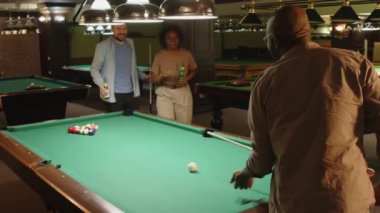 Barda farklı arkadaşlarla bilardo oynamaya başlarken bilardo topuna nişan alan Afrikalı Amerikalı adamın arka planı
