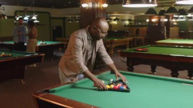Siyah adamın kulüpte çalışırken renkli bilardo toplarını üçgen piramidin içine attığı orta boy bir fotoğraf.