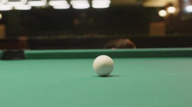 Bıyıklı şüpheli beyaz adam bilardo masasının arkasında belirdi ve bilardo topuna baktı. Maç sırasında top için doğru açıyı seçti.