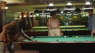 Siyahi adamın kulüpte çeşitli arkadaşlarla oynarken ve bira içerken bilardo topunu deliğe başarıyla batırdığı orta boy bir fotoğraf.