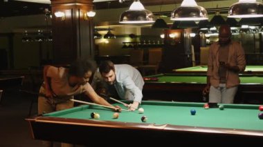 Beyaz adamın siyah bayan arkadaşına bilardo kulübünde bilardo toplarına nasıl nişan alınacağını ve nasıl vurulacağını öğretirken.