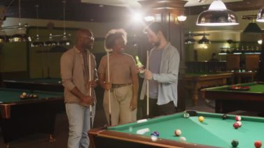 Akşamları bilardo kulübünde elinde ıstakayla poz veren üç farklı kadın ve erkek arkadaşın grup portresi.