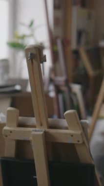 Ortalama dikey, hiç kimse vurulmamış, ressamlar tuvalle resim sehpası kurmuş, küçük, sıkışık bir sanat stüdyosunun ortasında, pencerenin yanında, gün ışığında.