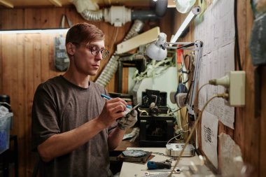 Not defterine not alan genç teknisyen, duvarın önünde elinde planlar ve ayrıntılı boyutları kontrol ederken...