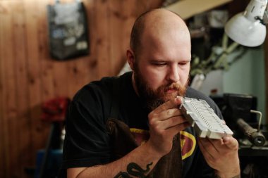 Plastik geri dönüşüm fabrikasının ciddi genç işçisi atölyedeki yeni metal parçaları veya kalıpların yüzeyine bakıyor