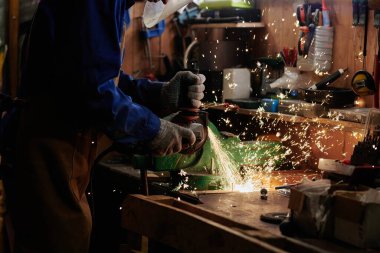 Koruyucu maskeli tanınmayan metal işçisinin elleri ve endüstriyel makinenin metal detaylarını öğüten eldivenler.