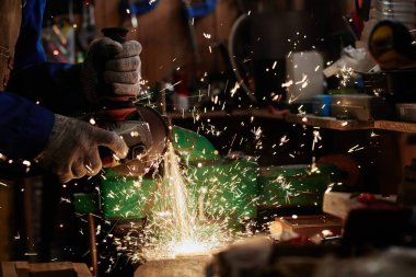 Tanımlanamayan koruyucu eldivenli erkek metal işçisi tezgahın yanında duruyor ve endüstriyel makinenin detaylarını öğütüyor.