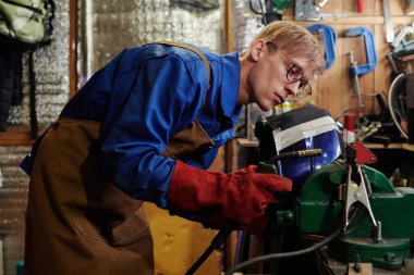 Kaynak makinesi tutan koruyucu eldivenli genç kaynakçı atölyede ya da fabrikada metal parçalarını bükerken