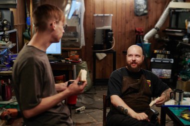 İki aç genç erkek teknisyen sandviç yerken birbirlerine bakıyorlar, çay içip çalışma noktalarını tartışıyorlar.