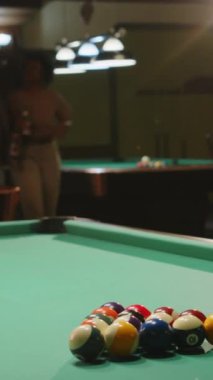 Afro-Amerikalı arkadaşları barda bira şişeleriyle ona ulaşırken, bilardo masasını bilardo masasına hazırlayıp bilardo toplarını kıran heyecanlı beyaz adamın dikey orta pozu.