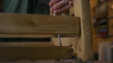 Atölyedeki eski ahşap sandalyeyi restore ederken tornavida kullanan yüzü olmayan zanaatkârın yakın plan çekimleri.