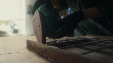Eldivenli yüzsüz marangozun, atölyedeki mobilyaları tamir ederken zımpara makinesiyle ahşap iskeleti parlatması.