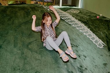 Kareli gömlekli, gri pamuklu çoraplı, modern oyun parkında yuvarlanan sevimli küçük kız.