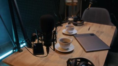 Stüdyoda duran profesyonel mikrofonun orta kavisli görüntüsü. Tanımlanamayan bir adam masaya oturuyor ve podcast senaryosunu kontrol ediyor.