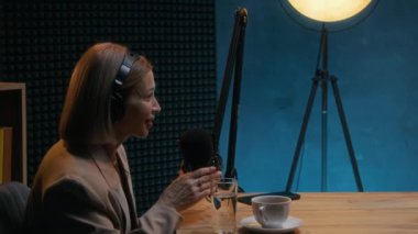 Orta ölçekli, orta yaşlı, beyaz bir iş kadınının mevcut ekonomi ve yatırım ortamı hakkında konuşurken stüdyoda podcast gösterisine katıldığı yavaş çekim.