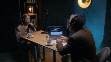 Yetişkin beyaz kadın girişimcinin küçük işletmeler için ekonomik zorluklar üzerine podcast 'te konuştuğu orta boy bir fotoğraf, erkek ev sahibi dinleme, dizüstü bilgisayarda çalışan ses karıştırma yazılımı