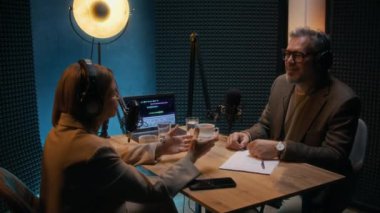 Orta yaşlı beyaz erkek gazeteci ve kadın konuk uzmanın podcast 'te ekonomi haberlerini tartışırken, önemli konularda anlaşırken, gülümserken ve yumruklarken, mavi arka planda