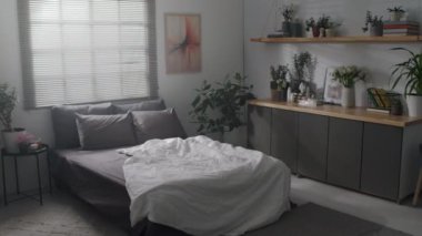 Gri ve beyaz gölgeli, geniş çift kişilik yataklı ve ev bitkileriyle dolu çok katlı tencereli rahat bir yatak odası olan hiç kimse yok.