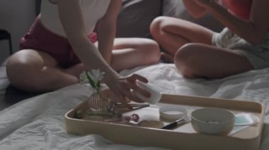 Cilt bakımı partisinde yeni güzellik ürünlerini test eden, vücut kremi ve serumu deneyen, kokuyu ve rahatlatıcıyı tartışan ev elbiseli genç ve çekici kadınların eğik çekimi.