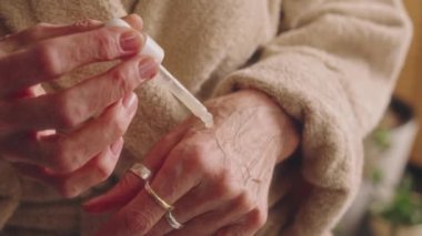 Bornozlu yaşlı bayanın duştan sonra ellerinde su serumu ve cilt bakımı uygulaması.