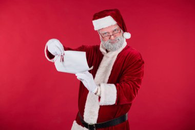 Noel Baba gibi giyinmiş yaşlı bir adam, uzun listeyi sıkı kırmızı arka planda tutuyor ve inceliyor. Beyaz eldivenli el gülümseyerek özel bir ismi işaret ediyor.