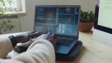 Ofiste yazılım üzerinde çalışırken siyah ekranda dizüstü bilgisayarda kod yazan isimsiz siyahi erkek programcının ellerinin orta derecede kapatılması, sonra da masaüstü bilgisayarında test edilmesi