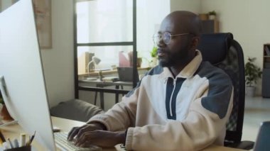 Orta ölçekte, kurumsal bilişim ofisindeki bilgisayar üzerinde fazla mesai yapan yorgun siyah erkek yazılım geliştiricisinin duraksaması, gözlükleri çıkarması ve onları masanın üzerine koyması.