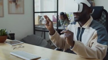 VR kulaklıklı neşeli Afrikalı Amerikalı erkek programcının internet taraması ya da artırılmış gerçeklik, çevirme ya da web sitelerinde elektronik dokümanların görüntülenmesi, sayfalara yakınlaşması.