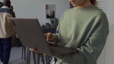 Ofiste duran Çinli kadın programcının orta ölçekli yakın çekimi, dizüstü bilgisayarda hızla bilgisayar kodu yazması, siyah erkek yöneticinin etrafta gezinmesi, cep telefonuyla müşteriyle proje tartışması.