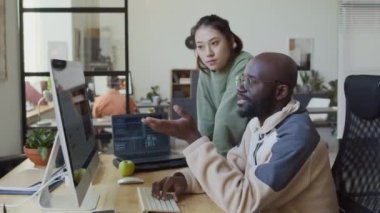 Genç Afrikalı Amerikalı erkek programcının bilgisayar ve dizüstü bilgisayarın önünde oturmuş yeni yazılımları test ederken orta ölçekli bir fotoğrafı.