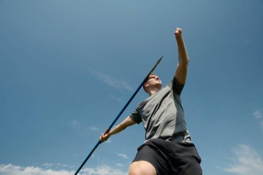 Açık hava spor müsabakaları sırasında açık gökyüzü altında atılacak cirit ve tekniğe odaklanmış bir atlet.