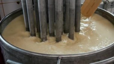 Pişirme işlemi sırasında ısıtılmış metal fıçıda tahta kürekle süt karıştıran tanınmayan peynir fabrikası işçisinin elleri kapalı.