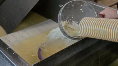 Küçük bir zanaatkar fabrikasında, metal lavaboda süt suyu çekerken borunun altında süzgeç tutan tanınmayan bir erkek peynir üreticisinin eli yakın plan.