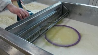 Metal lavaboda yeni pişmiş lor peyniri süzen ve kütle ile kepçeyle sıkıştıran tanınamaz haldeki zanaatkar peynirin orta derecede yakın çekimi.