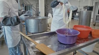 Kafkas erkek ve kadın fabrika çalışanlarının sıcak suya elastik peyniri bandırıp örgü şeklinde sarmaladığı orta boy bir fotoğraf.