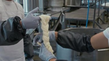 Peynir kurdeleleri tutan tanınmayan peynir üreticisinin elleri ve örgü şeklindeki iş arkadaşı paketlemesi fabrikada zanaatkar gıdalar üretirken sona eriyor.