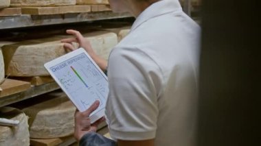 Beyaz üniformalı beyaz kadın teknolojinin orta boy arka planı. Fabrikadaki yaşlanma odasında dijital tablet duruyor. Rafta olgunlaşan peynirleri inceliyor.