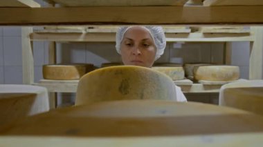 Rafların arkasından kadın fabrika işçisinin olgunlaşma odasında raflarda yürüdüğü, peynir çarkıfeleğini bulduğu, kabuğu çıkardığı, kabuğu geri koyduğu orta büyüklükteki kapatma sahnesi.