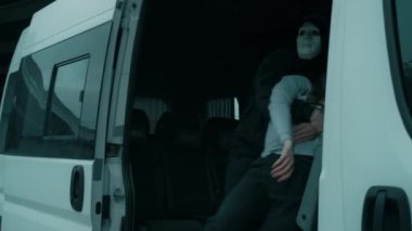 Maskeli, kimliği belirsiz bir erkek manyağın, baygın bir kadını minibüse bindirip, etrafa bakınıp, kapıyı kapatırken, kızı kaçırırken çekilmiş bir fotoğrafı.