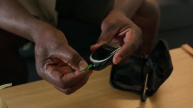 Siyah adamın kan şekeri seviyesini evde ölçmeye hazırlanırken kan şekeri monitörüne test bandı yerleştirdiği görüntüyü kapat.