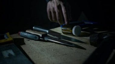Tanımlanamayan katilin eli karanlık odada cinayet silahını seçerken masadan keskin bir bıçak alıp kontrol ediyor.